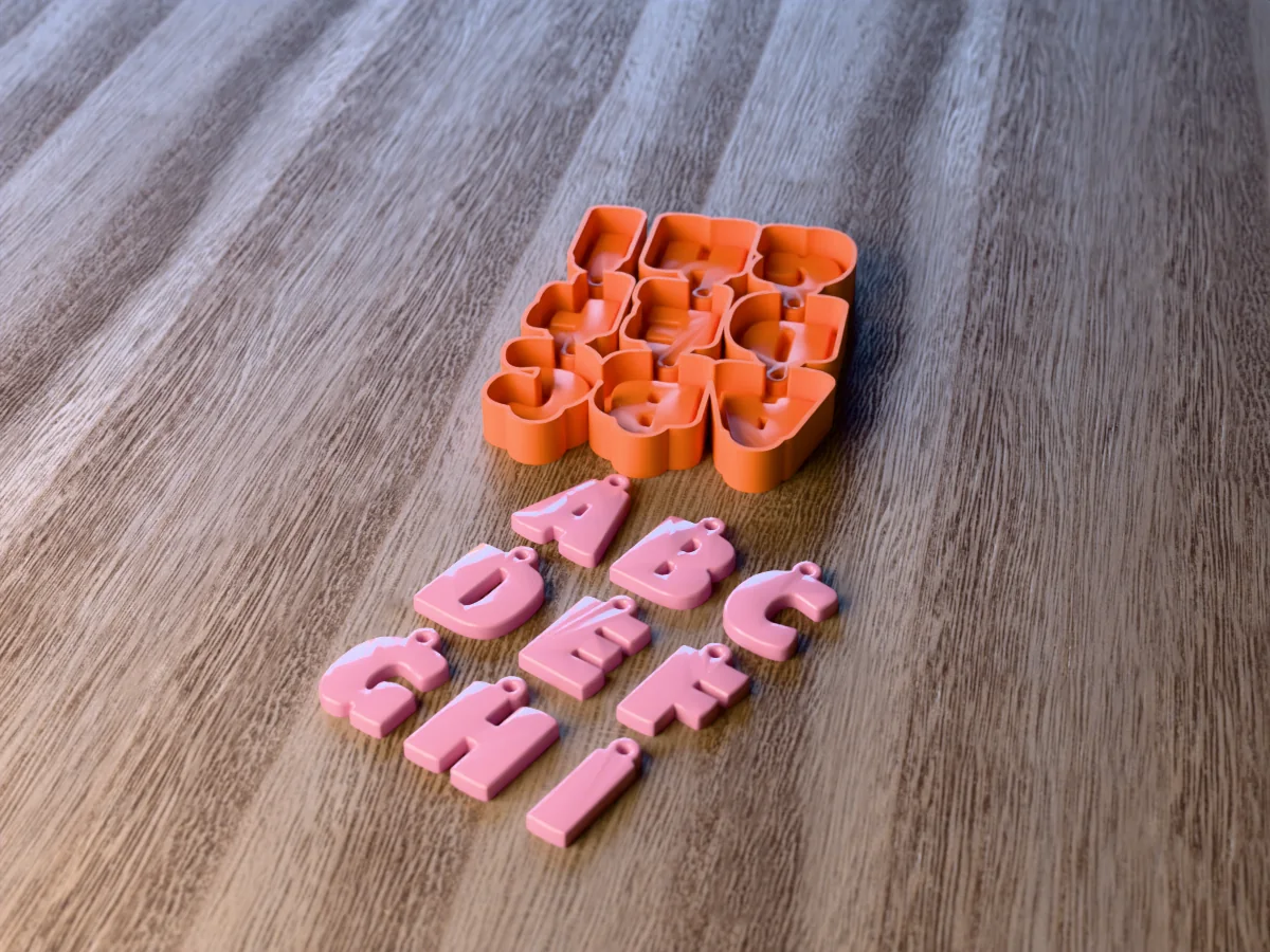 3D render of the printed caster for an alphabet resin keychain mold with the letters A to I, and nine pink bubble letter keychains with ring tabs in front