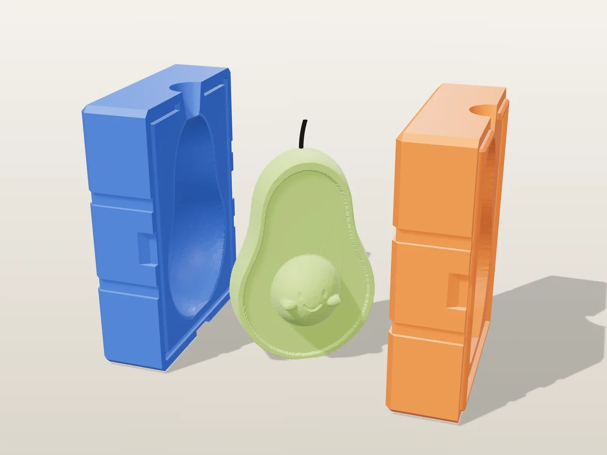 3D render of a green avocado half candle with a smiling face on its pit between the two printed halves of its rigid blue and orange mold