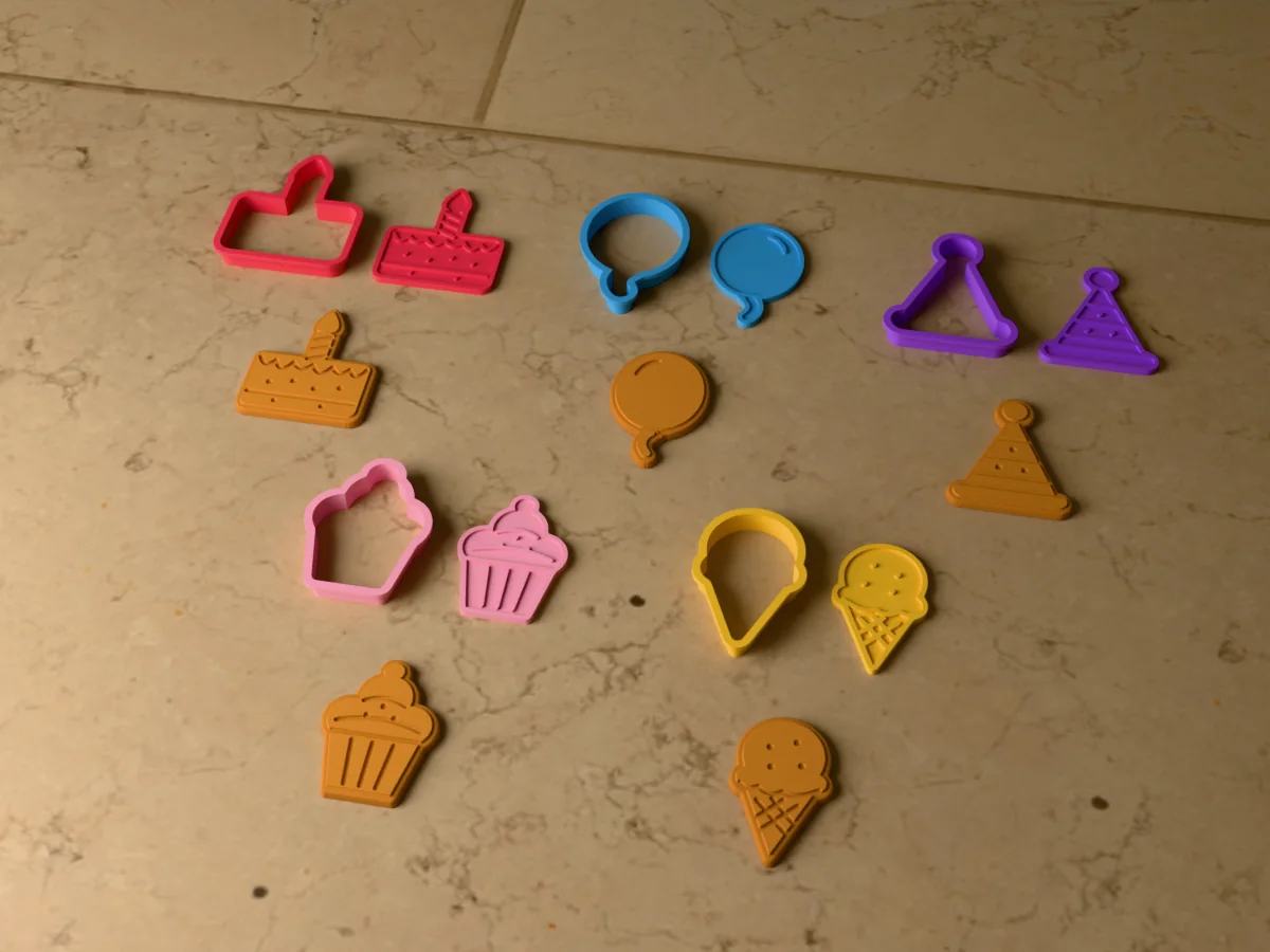 3D render of five 3D-printed birthday cookie cutters with their stamps and a golden stamped cookie in front of each: birthday cake, balloon, party hat, cupcake and ice cream cone