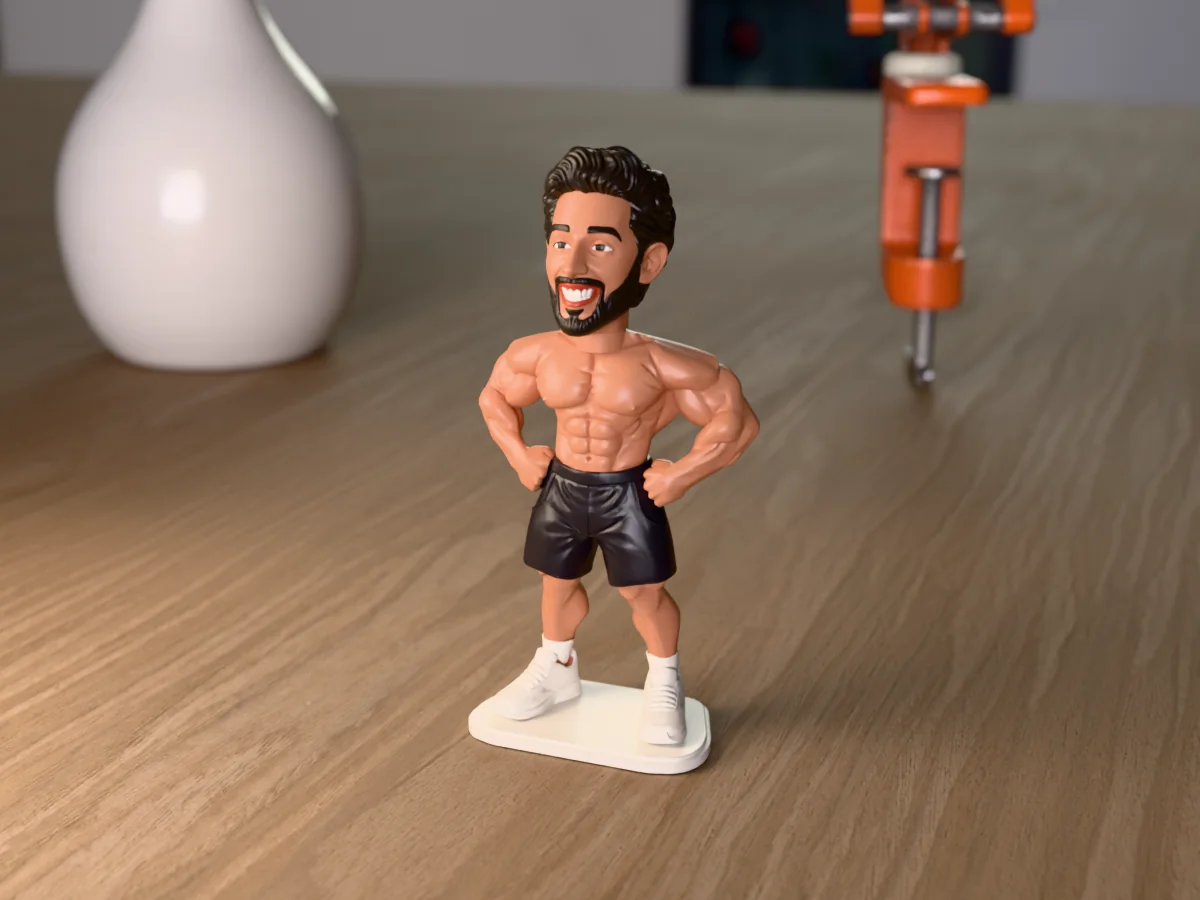 3D render of a 3D-printed mini figure of a guy with short black hair and a trimmed black beard, painted in 5 colours, on a table