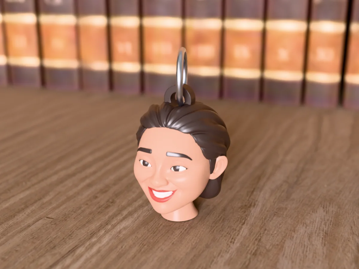 3D render of a 3D-printed head keychain of a smiling woman with a dark bob, painted in 6 colours, on a table