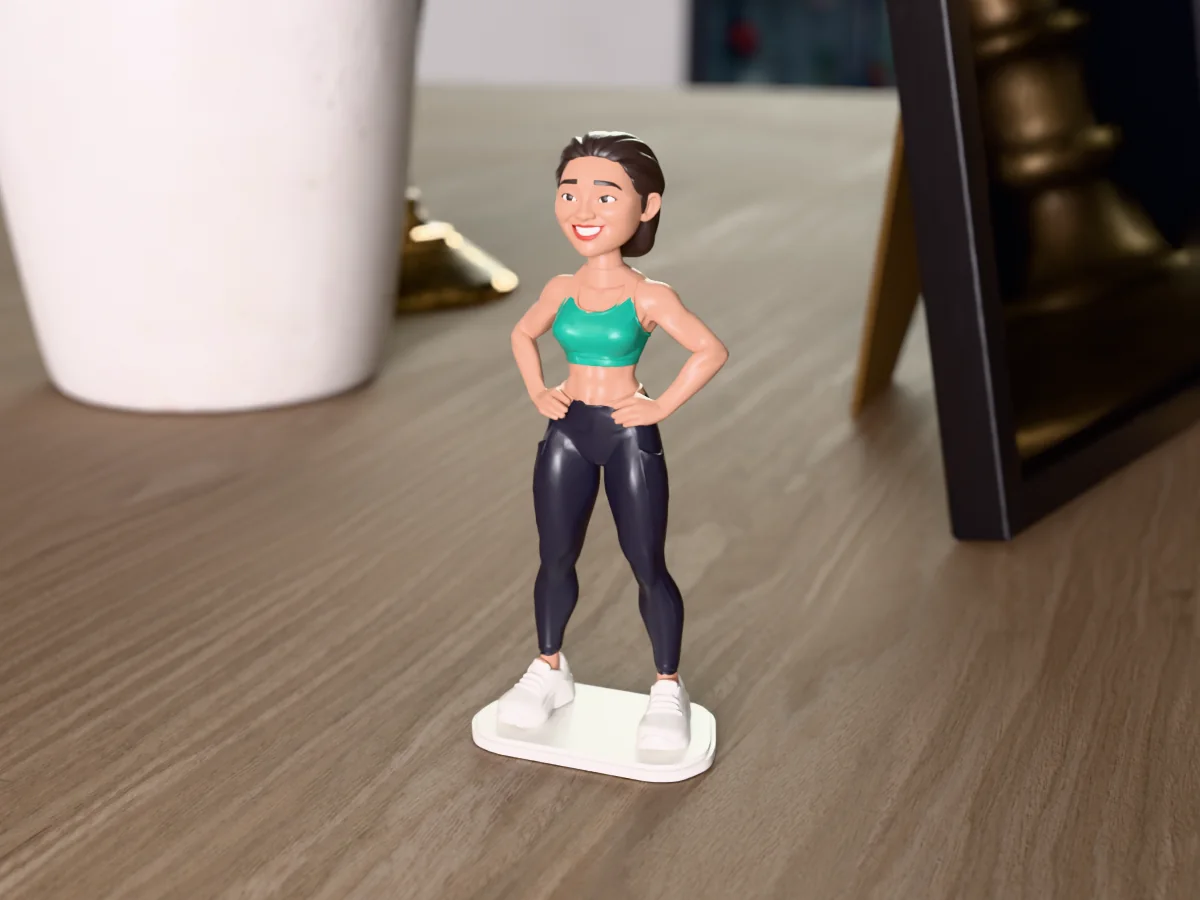 3D render of a 3D-printed mini figure of a smiling woman with a dark bob, painted in 6 colours, on a table