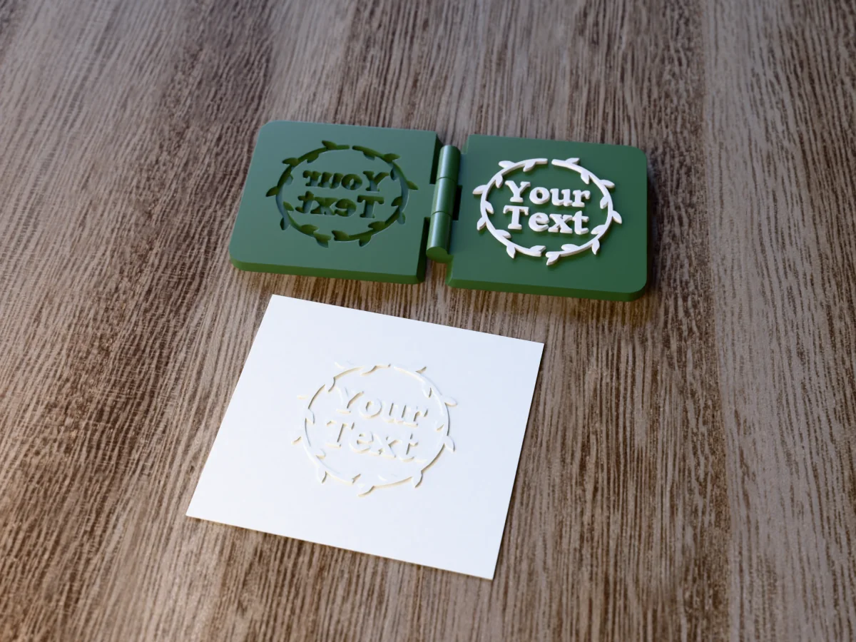 3D render of the printed botanical wreath embosser, open flat on its hinge, with the raised die and the matching cavity, next to a card embossed with its mark