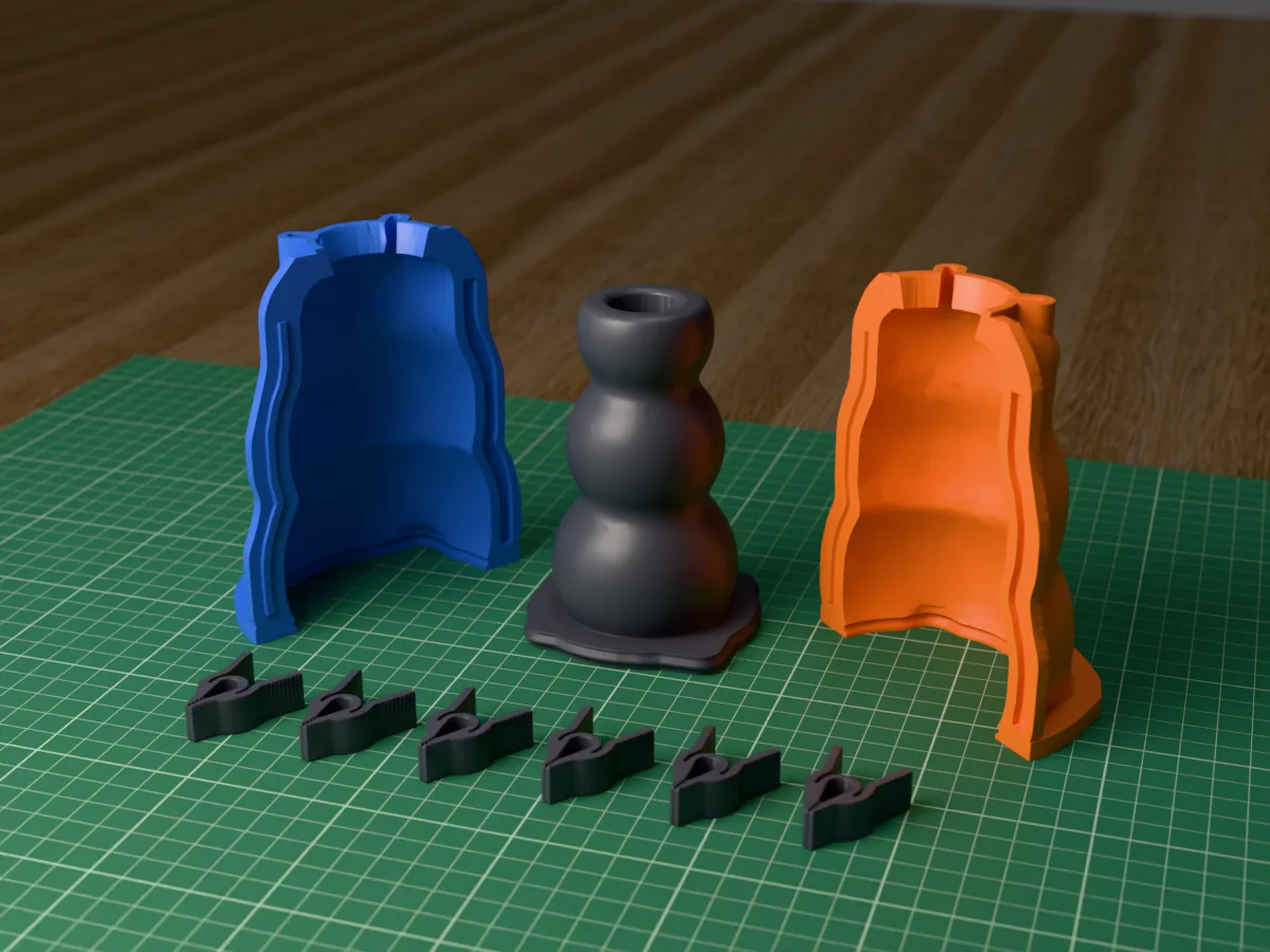 3D render of the bubble taper candle holder master, three stacked spheres with a candle socket, fused on its printed charcoal base between the orange and blue shell halves, with the charcoal clamps in front