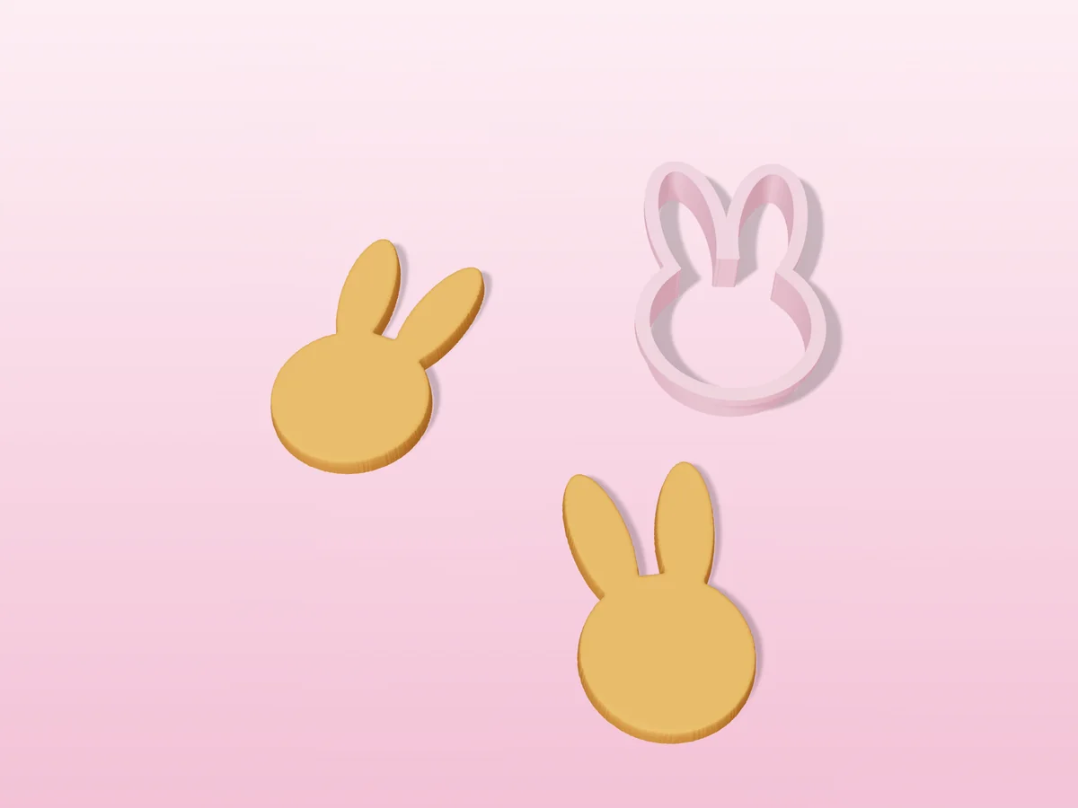 3D render of a light pink 3D-printed bunny cookie cutter next to two golden baked cookies in the same shape