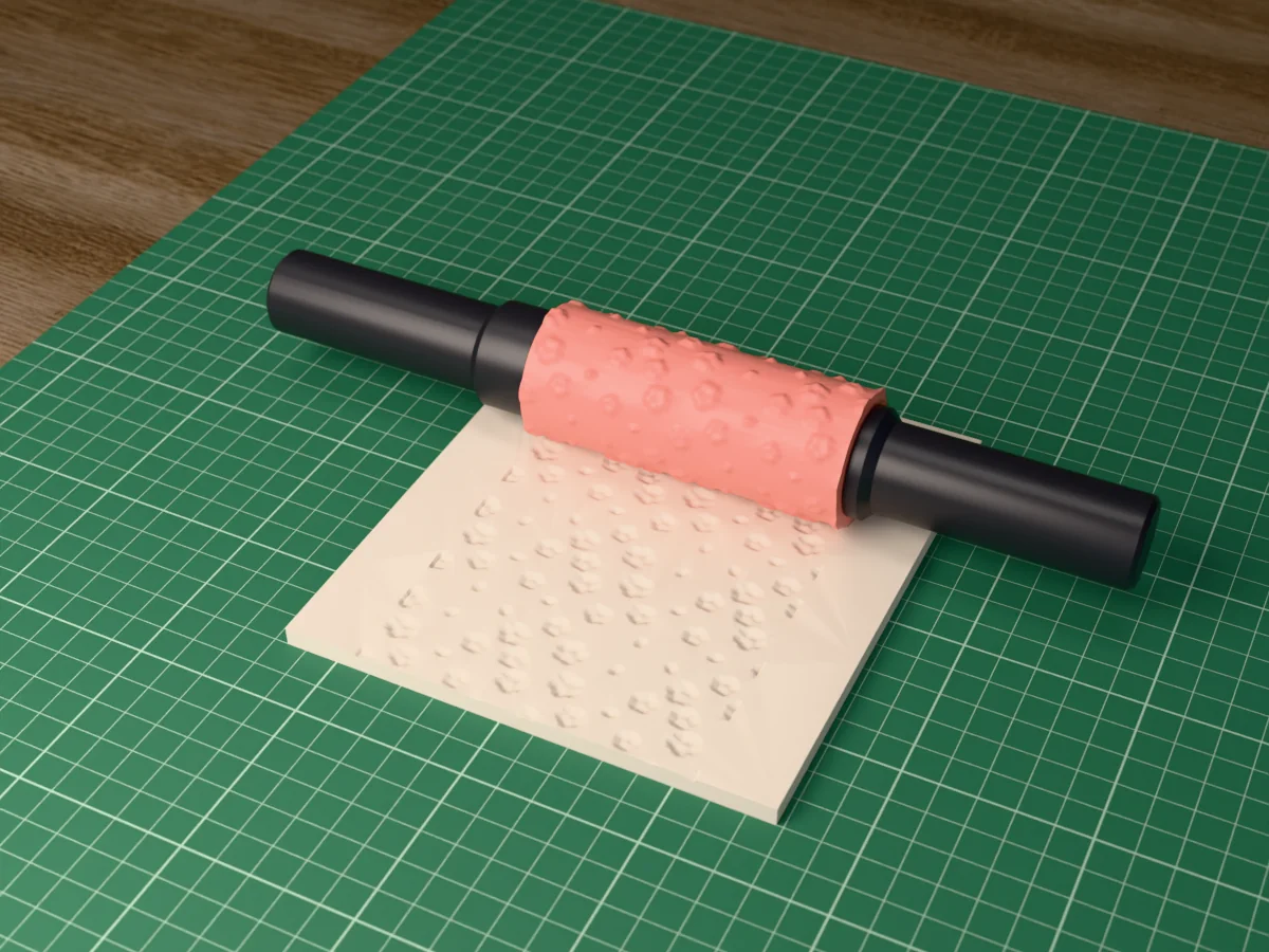 3D render of the printed cherry blossom textured rolling pin, its patterned sleeve between two dark handles, resting on a slab of clay it has pressed with cherry blossom