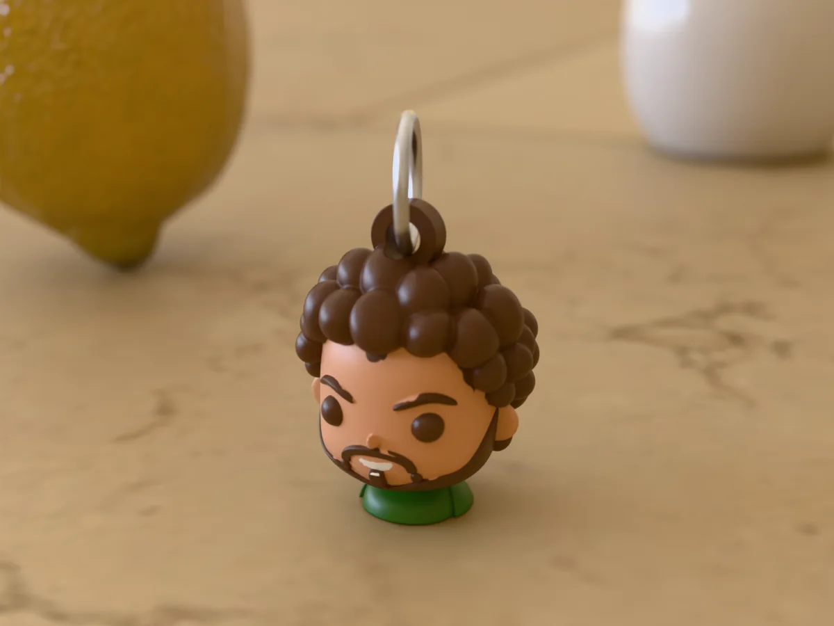 3D render of a 3D-printed head keychain of a big-eyed chibi version of a bearded guy with curly hair, painted in 6 colours, on a table
