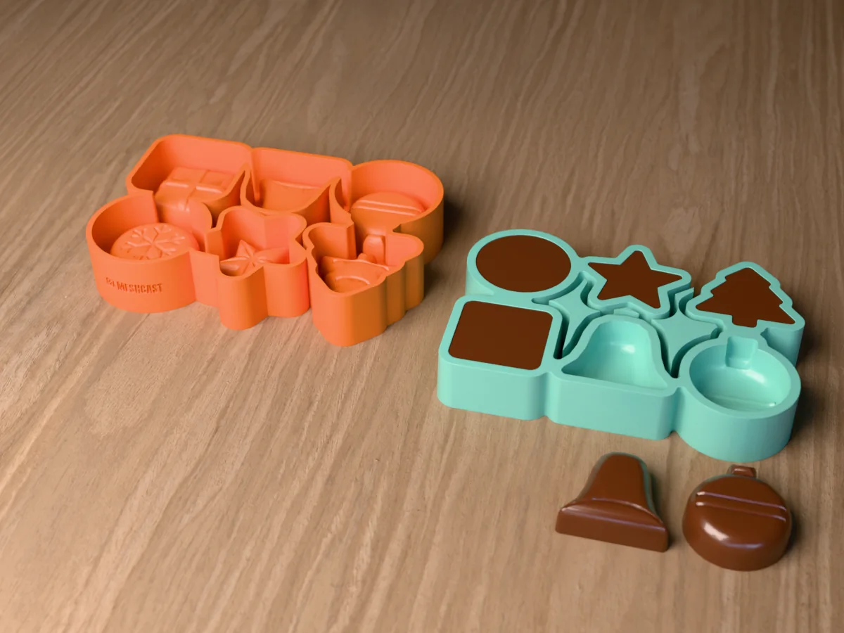 3D render of an orange printed caster beside a green silicone Christmas chocolate mold filled with chocolate, with a chocolate bell and bauble in front