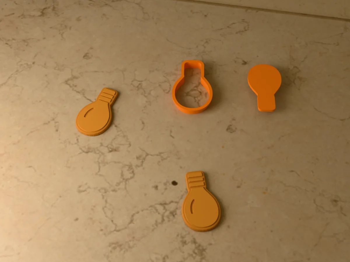3D render of an orange 3D-printed Christmas light cookie cutter and stamp next to two golden baked cookies with the screw cap and a shine line pressed in