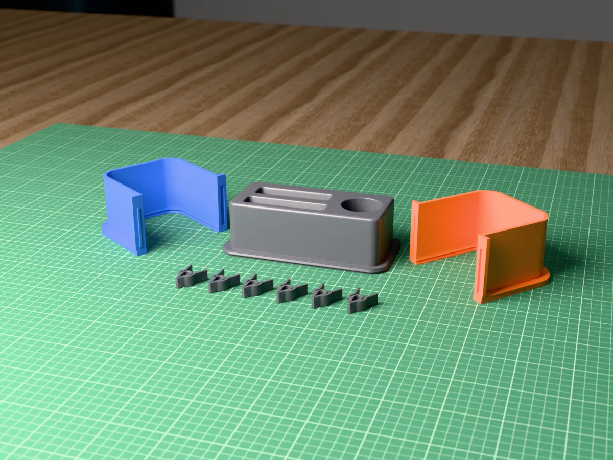 3D render of the concrete desk organizer master with a pen cup, a phone slot and a card slot, fused on its printed charcoal base between the orange and blue shell halves, with the charcoal clamps in front
