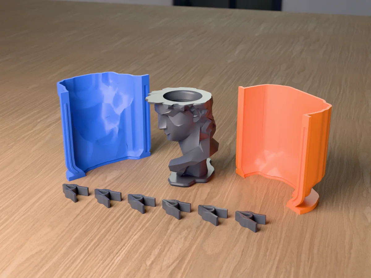 3D render of the low poly David head planter master with flat facets and a hollowed crown, fused on its printed charcoal base between the orange and blue shell halves, with the charcoal clamps in front