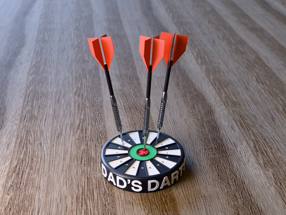3D render of the printed personalized dart holder: a round black case with DAD'S DARTS raised in white round its side, a black and white dartboard face with a green ring and red bullseye, and three darts standing in it