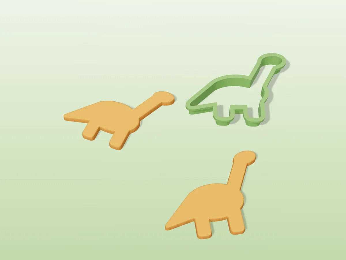 3D render of a green 3D-printed dinosaur cookie cutter next to two golden baked cookies in the same shape