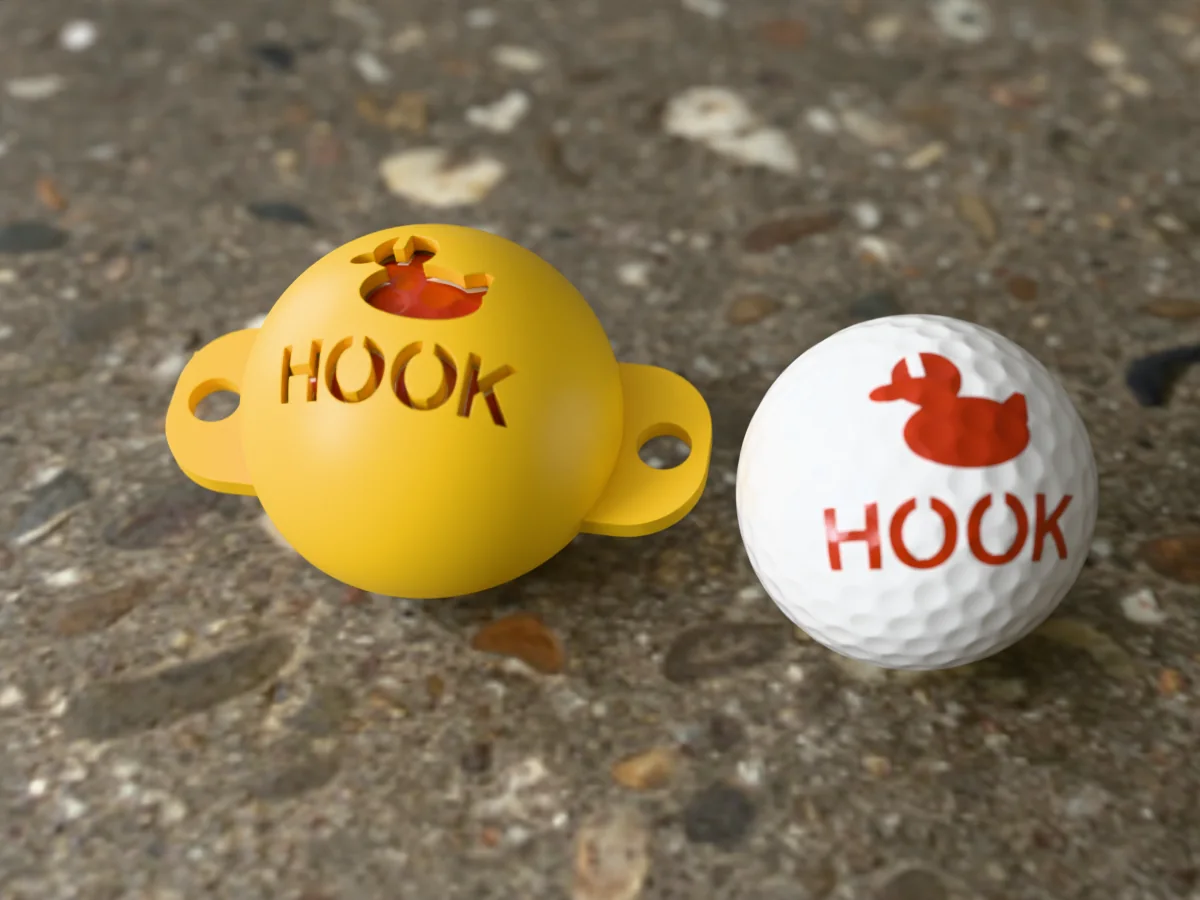 3D render of a yellow 3D-printed golf ball stencil with a duck over HOOK cut through it, sitting on a golf ball, next to a ball marked with a duck over HOOK in orange