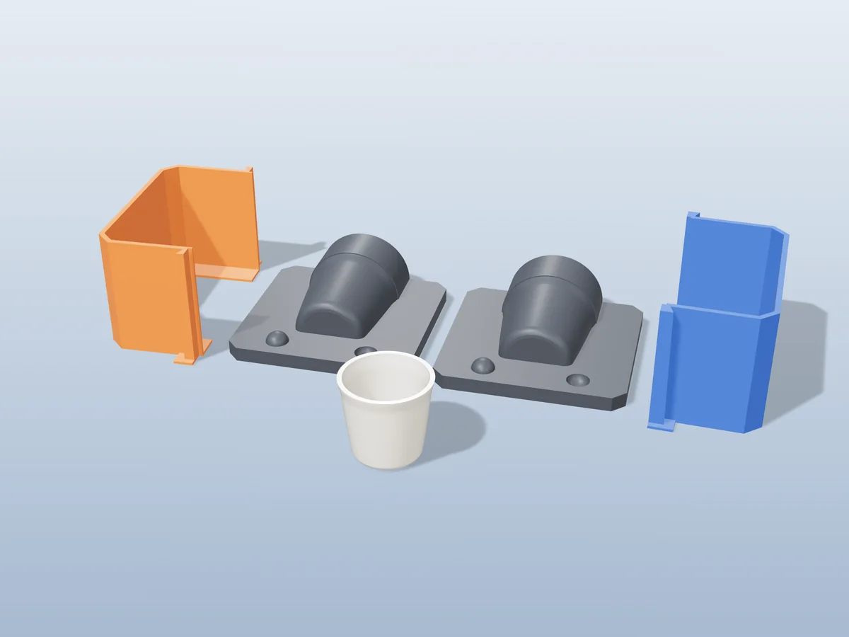 3D render of two printed plaster-mold housings for an espresso cup, orange and blue shells beside charcoal bases, with a white fired espresso cup in front