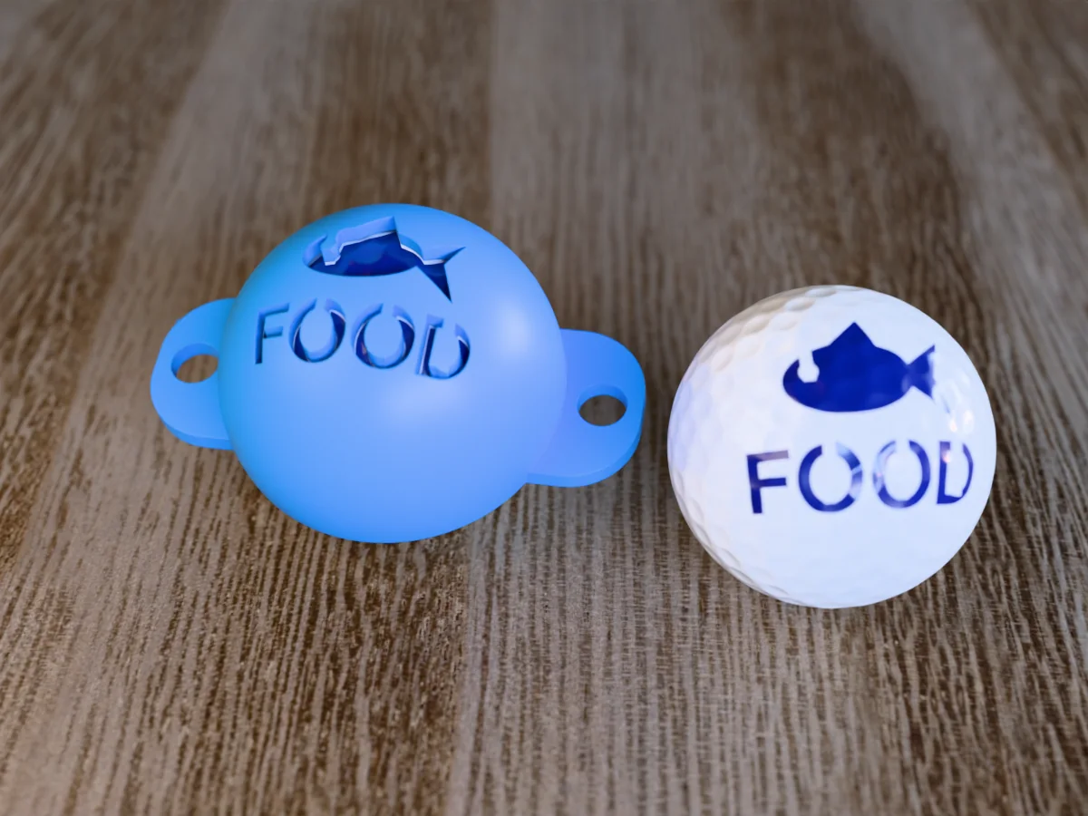 3D render of a blue 3D-printed golf ball stencil with a fish over FOOD cut through it, sitting on a golf ball, next to a ball marked with a fish over FOOD in blue