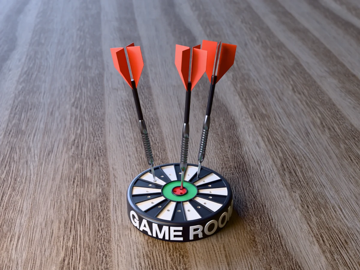 3D render of the printed personalized dart holder: a round black case with GAME ROOM raised in white round its side, a black and white dartboard face with a green ring and red bullseye, and three darts standing in it