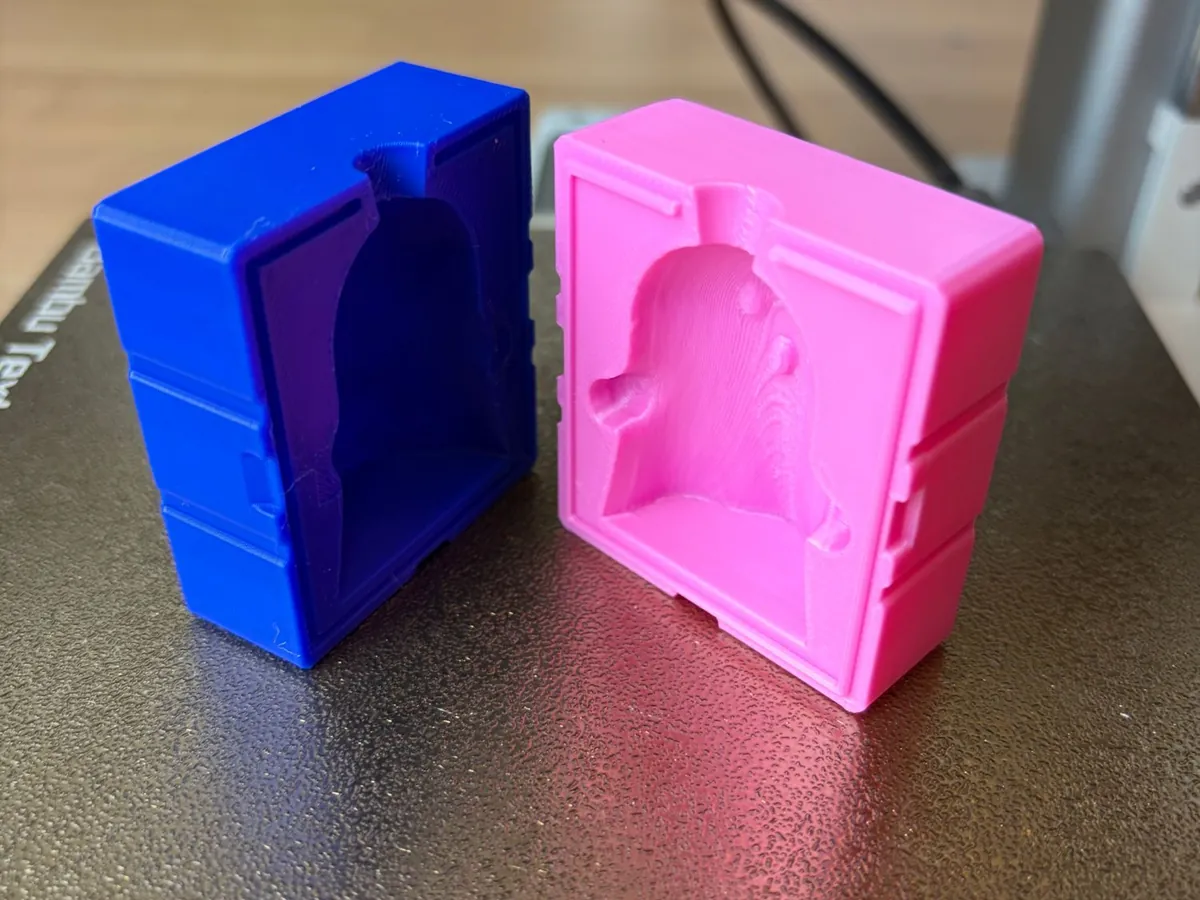 The two printed halves of the ghost candle mold, one blue and one pink, standing open on a printer bed with the ghost cavity facing up