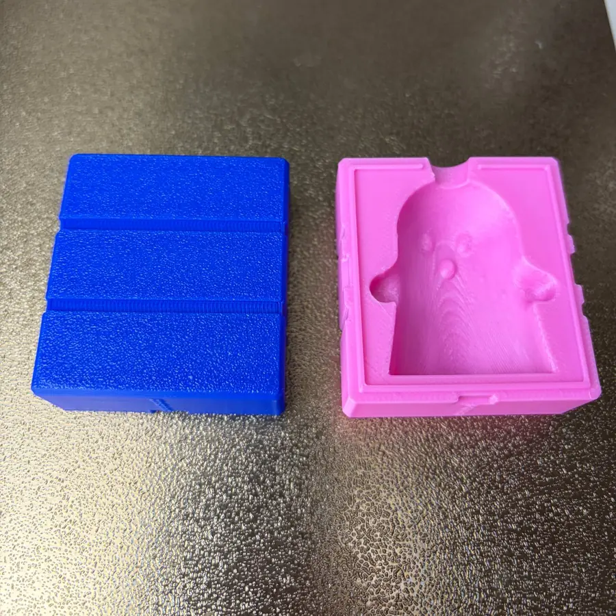 Outside of the blue ghost mold half with its two rubber-band grooves, next to the open pink half