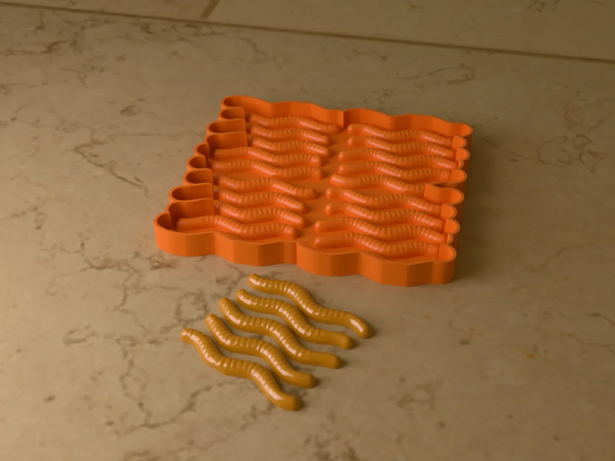 3D render of the printed caster for a twenty-cavity silicone gummy worm mold, with five orange gummy worms in front