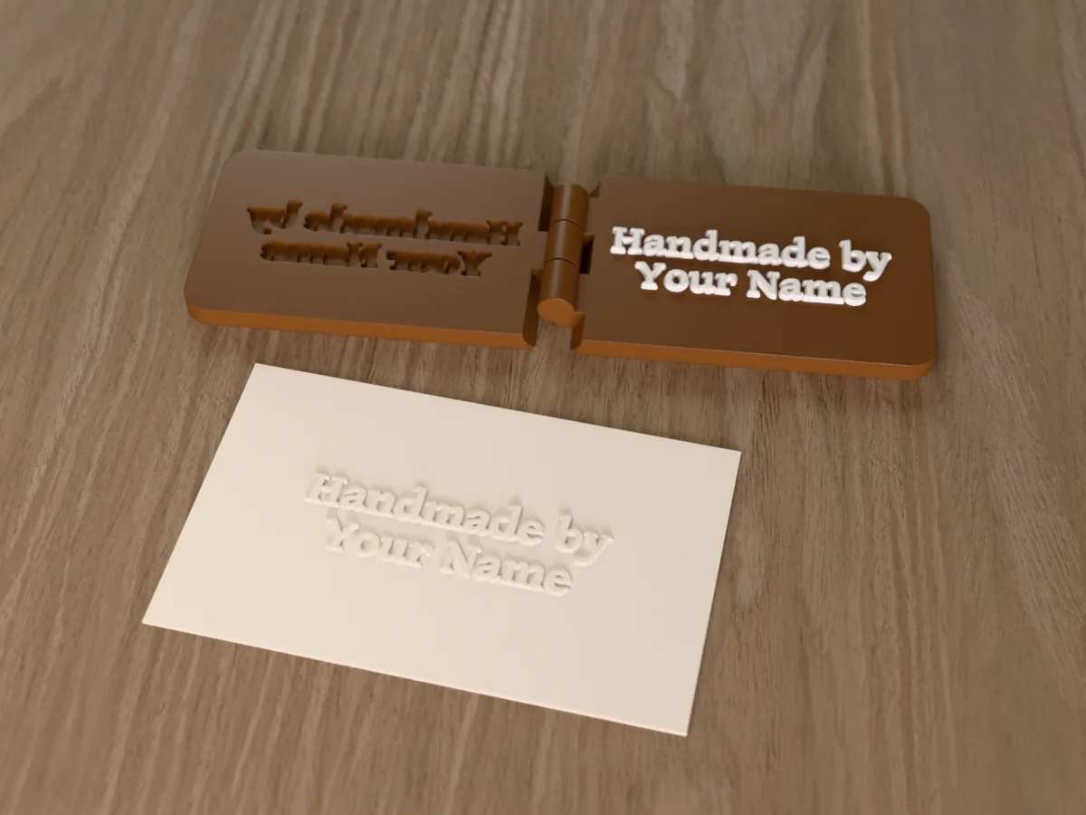 3D render of the printed handmade by embosser, open flat on its hinge, with the raised die and the matching cavity, next to a card embossed with its mark