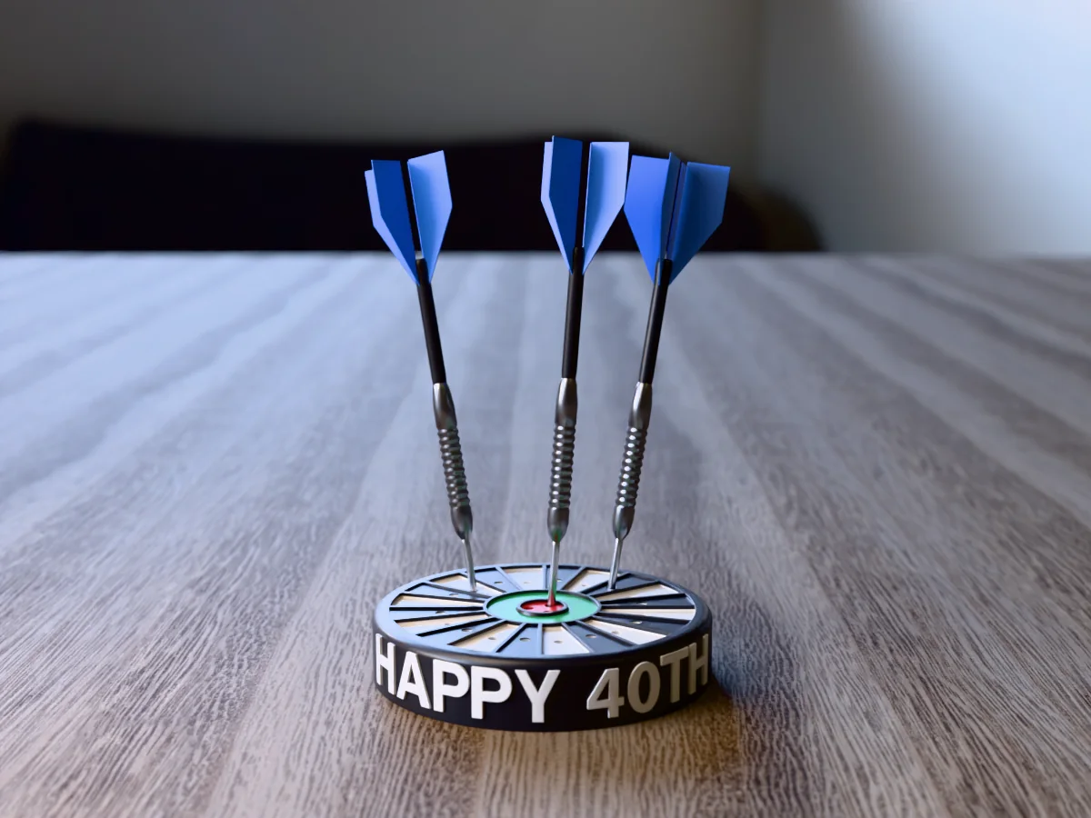 3D render, low view of the printed HAPPY 40TH dart holder on a table, the name raised in white round the black case and three darts with blue flights standing in it