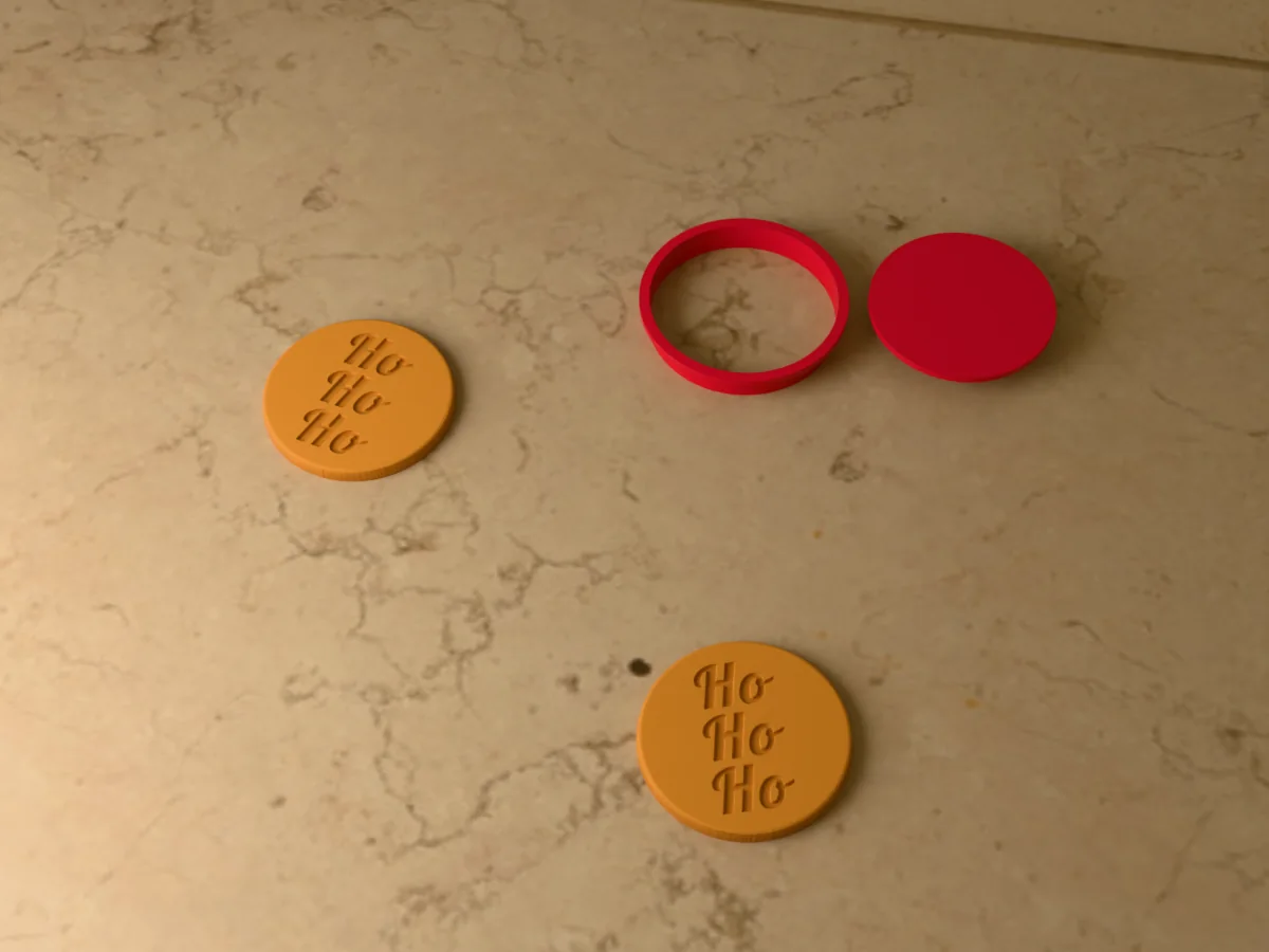 3D render of a red 3D-printed round cookie cutter and Ho Ho Ho stamp next to two golden baked cookies with Ho Ho Ho pressed in