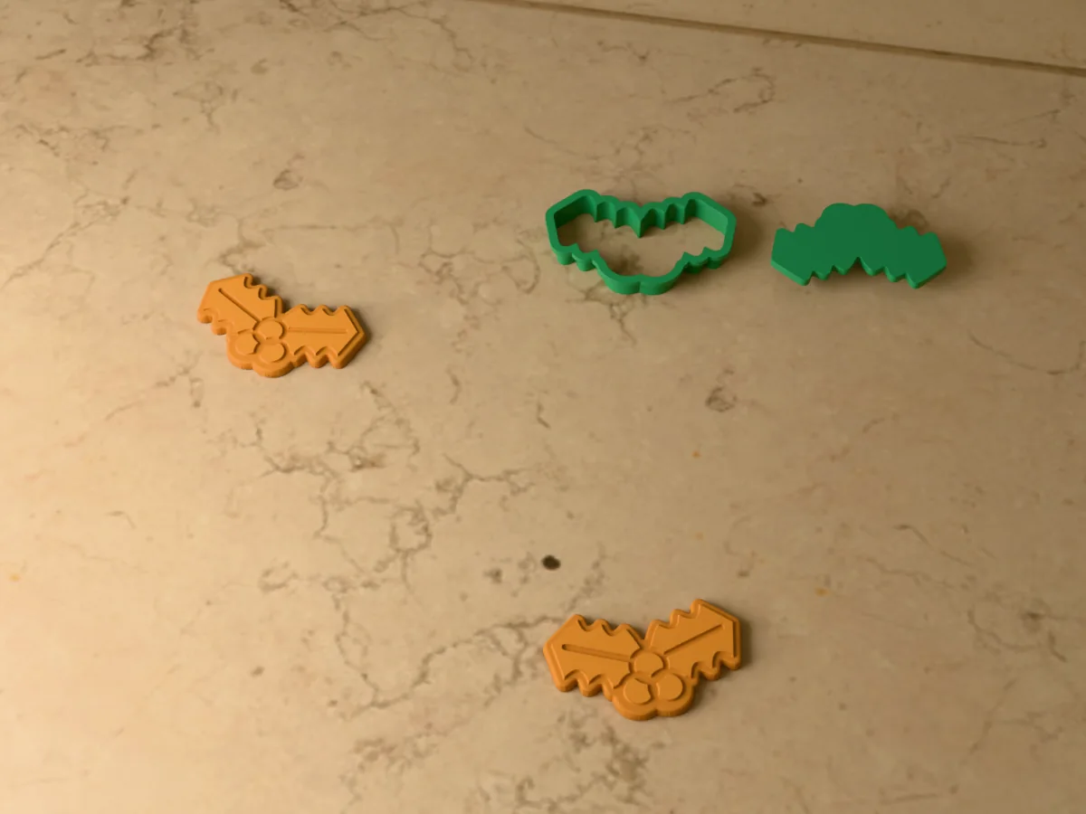 3D render of a green 3D-printed holly cookie cutter and stamp next to two golden baked cookies with the leaf veins and berries pressed in
