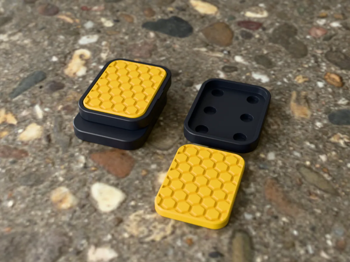 3D render of a charcoal and gold 3D-printed magnetic fidget slider with a honeycomb texture, assembled, next to a spare plate and insert