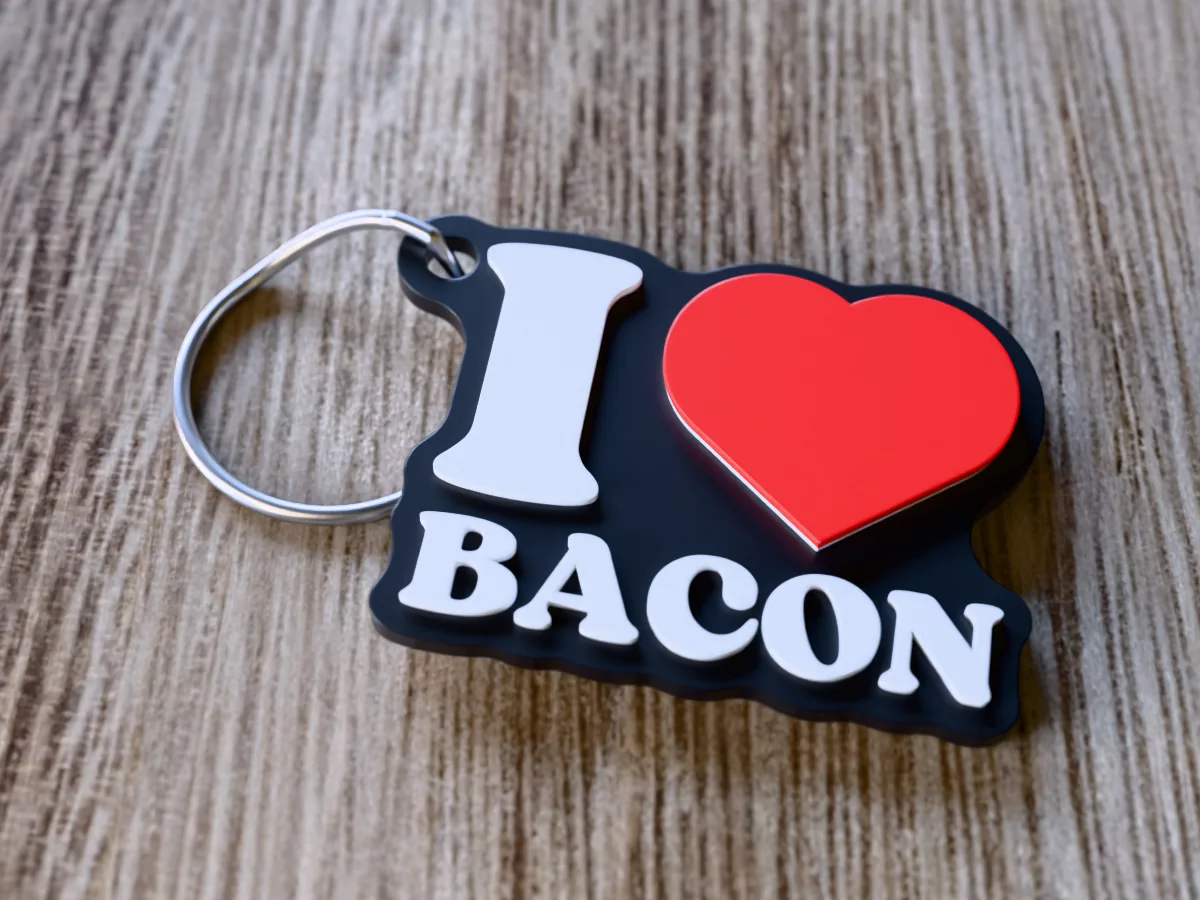 3D render of a black, white and red 3D-printed I love bacon keychain with a steel split ring through its hole