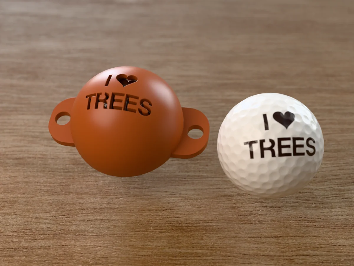 3D render of a brown 3D-printed golf ball stencil with I (heart) TREES cut through it, sitting on a golf ball, next to a ball marked with I (heart) TREES in dark brown