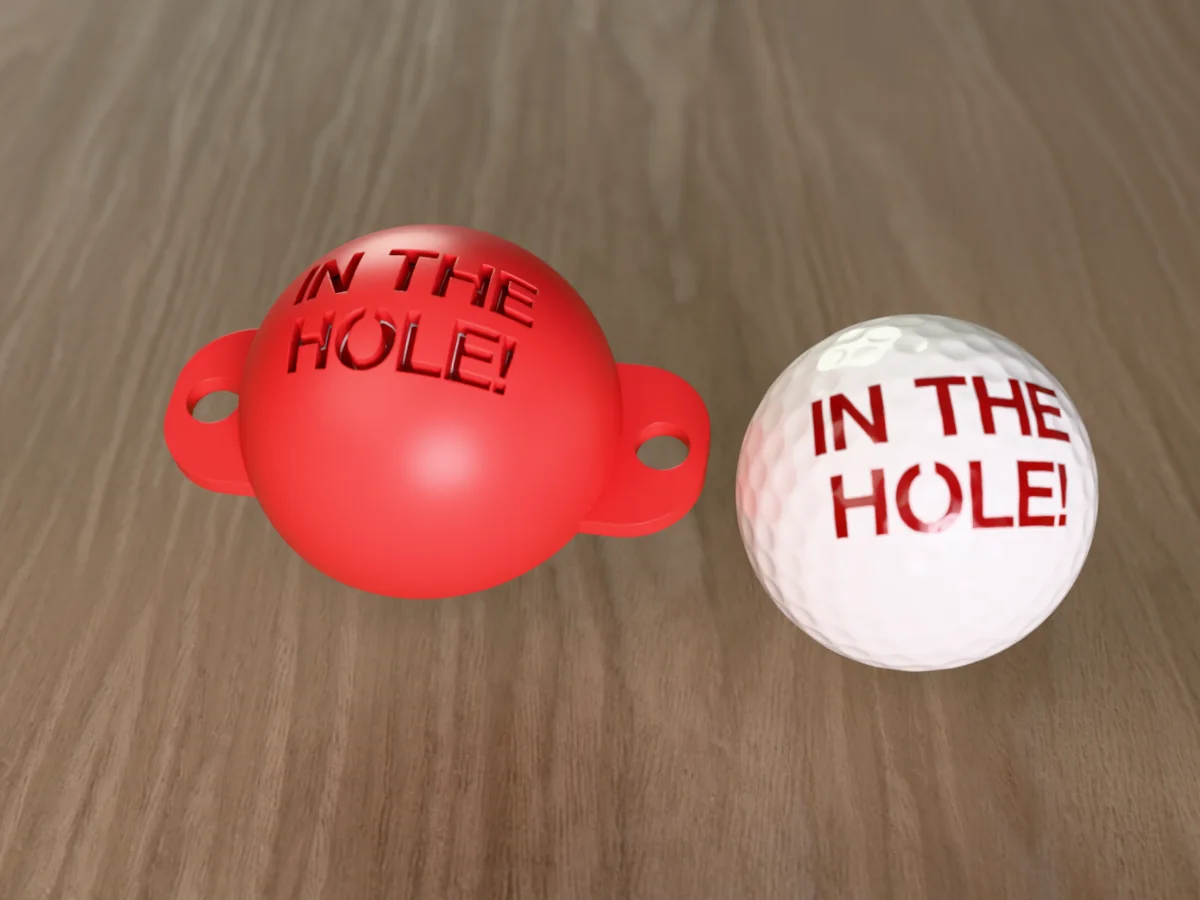 3D render of a red 3D-printed golf ball stencil with IN THE HOLE! cut through it, sitting on a golf ball, next to a ball marked with IN THE HOLE! in red