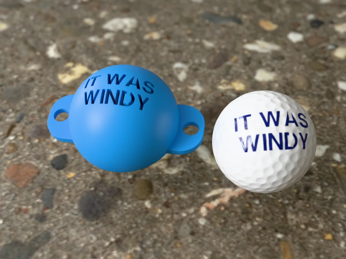 3D render of a blue 3D-printed golf ball stencil with IT WAS WINDY cut through it, sitting on a golf ball, next to a ball marked with IT WAS WINDY in blue