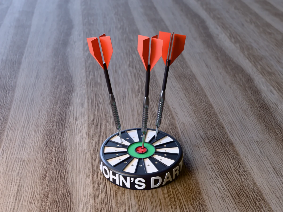 3D render of the printed personalized dart holder: a round black case with JOHN'S DARTS raised in white round its side, a black and white dartboard face with a green ring and red bullseye, and three darts standing in it