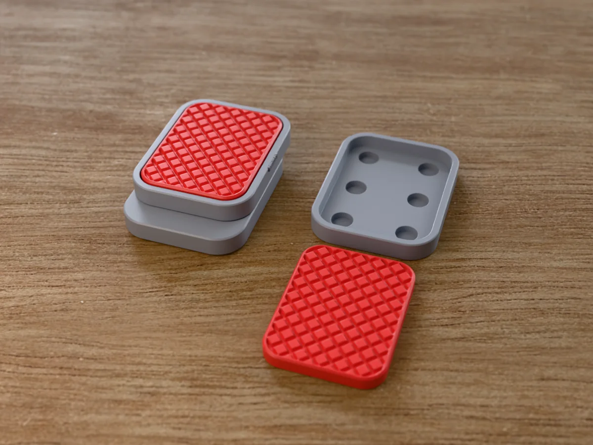 3D render of a grey and red 3D-printed magnetic fidget slider with a knurl texture, assembled, next to a spare plate and insert