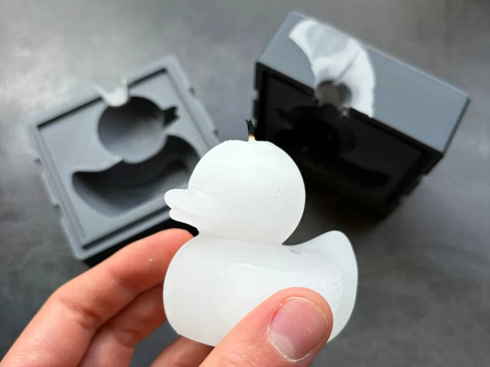 Photo of the finished white rubber duck candle held in a hand, its mold halves behind it