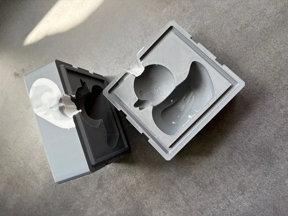Photo of the two halves of a 3D-printed rubber duck candle mold, opened after a pour, wax still on the pour spout