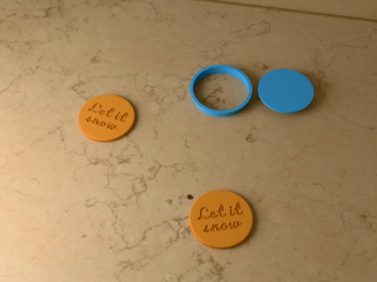 3D render of a light blue 3D-printed round cookie cutter and Let it snow stamp next to two golden baked cookies with Let it snow pressed in