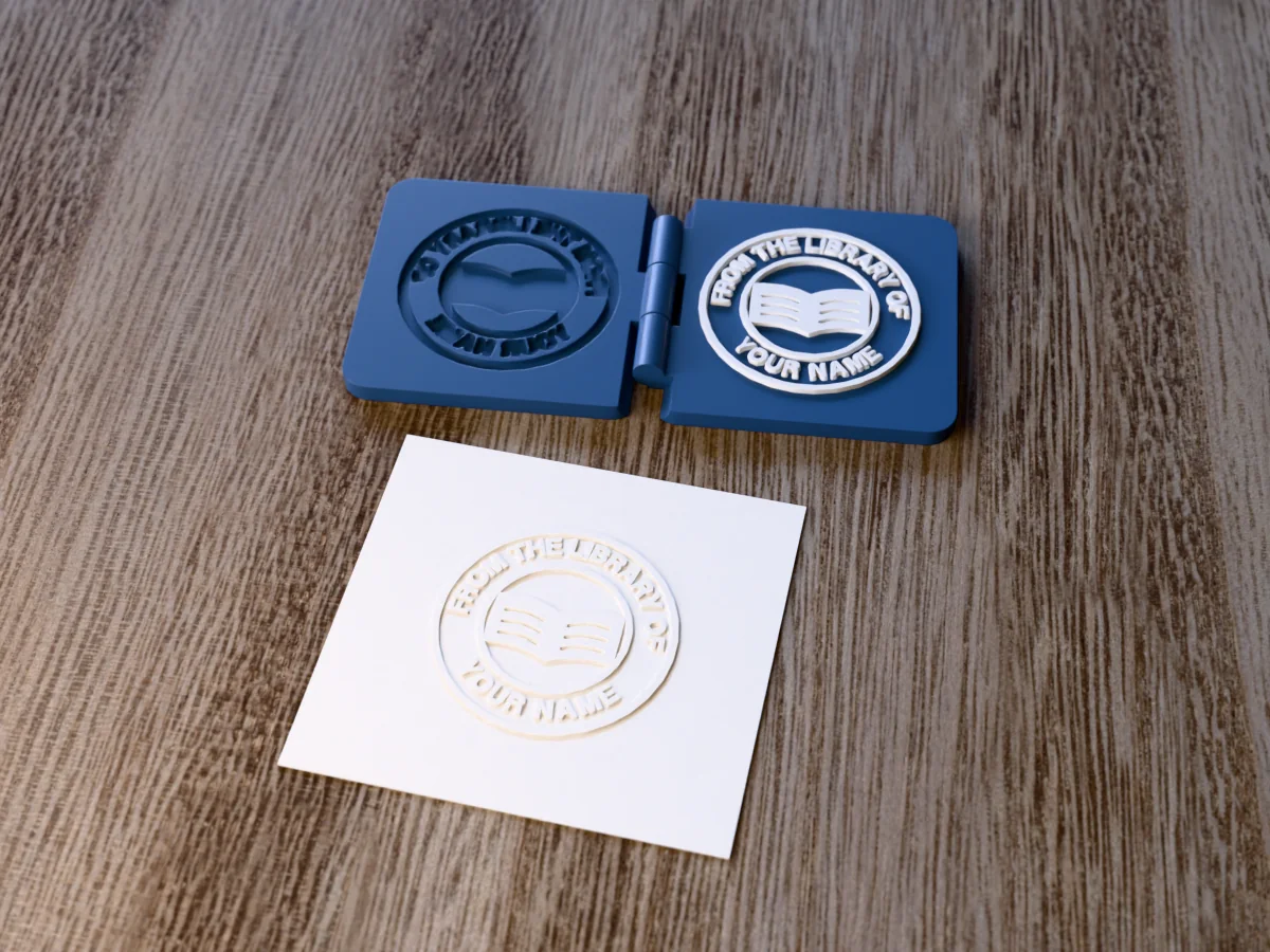 3D render of the printed library embosser, open flat on its hinge, with the raised die and the matching cavity, next to a card embossed with its mark