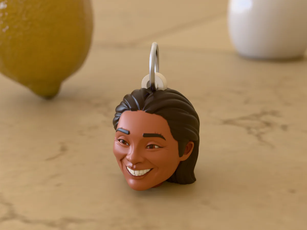 3D render of a 3D-printed head keychain of a beaming woman with long dark wavy hair, painted in 6 colours, on a table