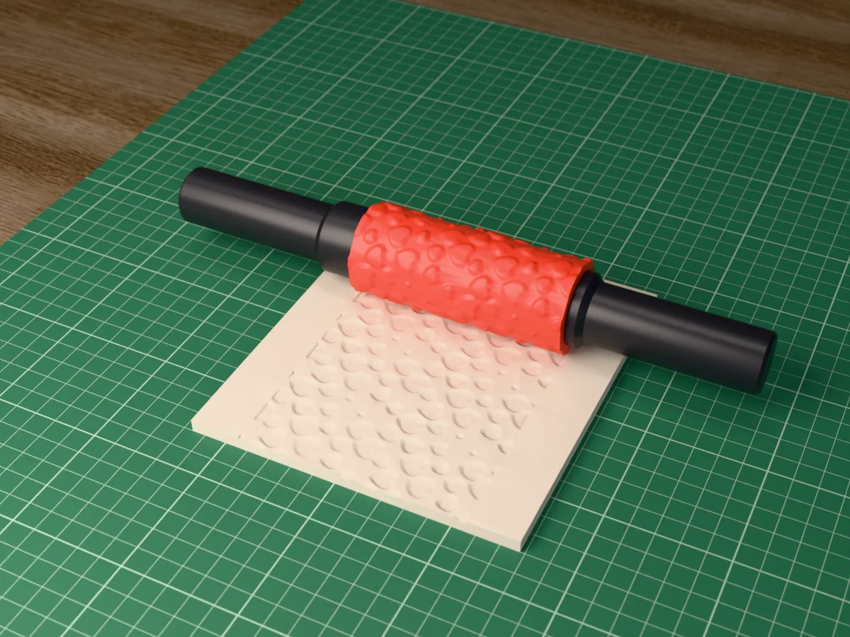 3D render of the printed love heart textured rolling pin, its patterned sleeve between two dark handles, resting on a slab of clay it has pressed with scattered hearts