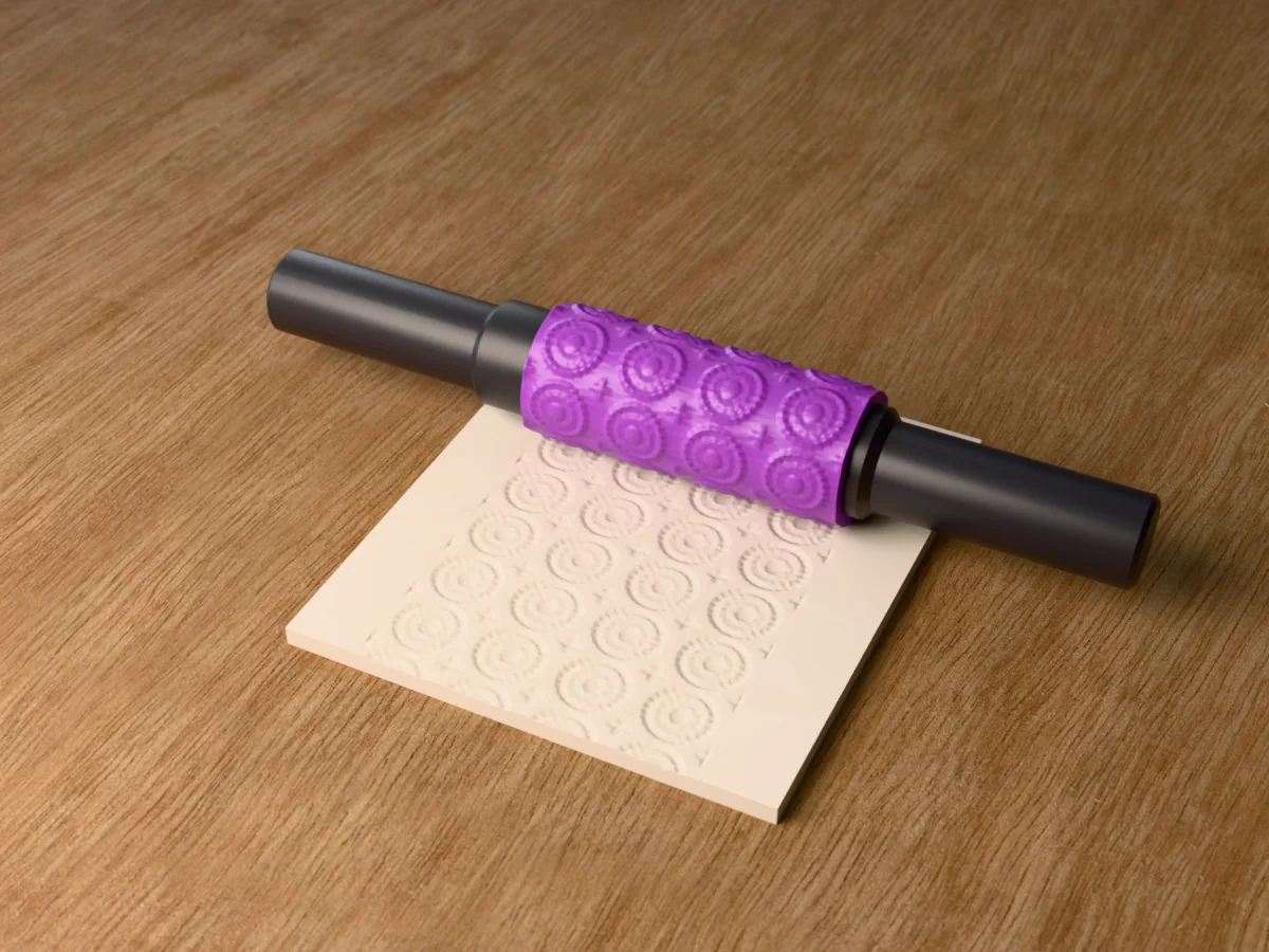 3D render of the printed mandala textured rolling pin, its patterned sleeve between two dark handles, resting on a slab of clay it has pressed with mandala rosettes