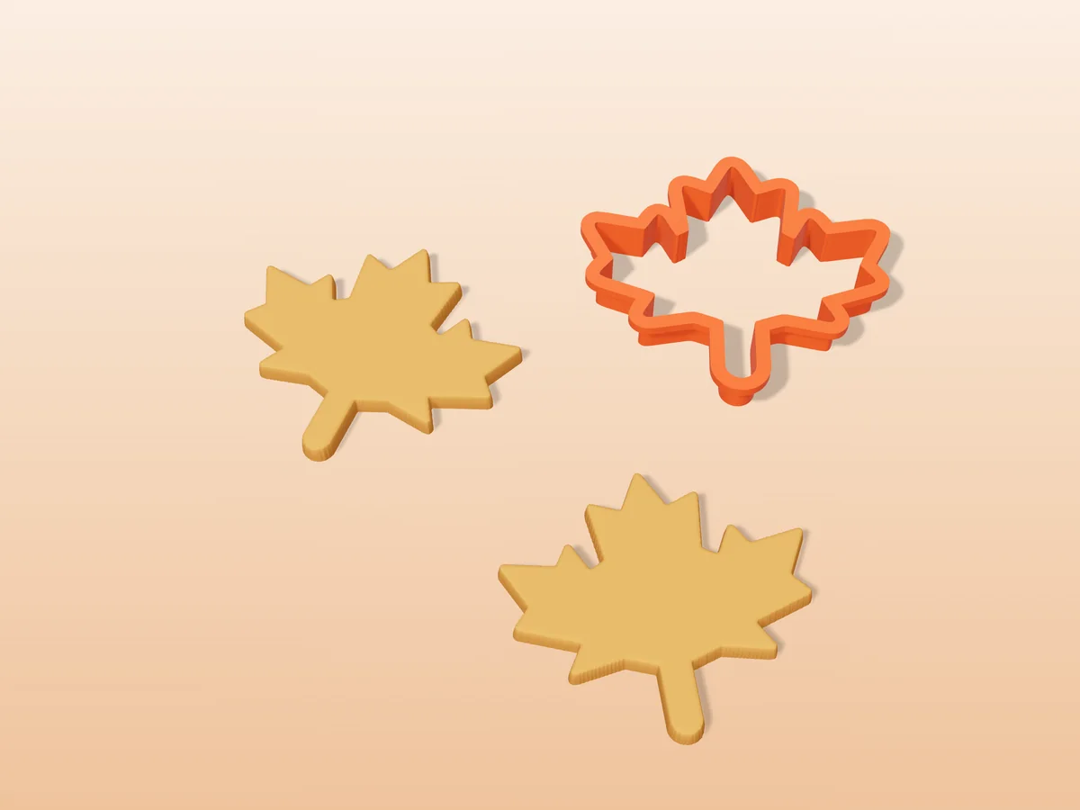 3D render of an orange 3D-printed maple leaf cookie cutter next to two golden baked cookies in the same shape