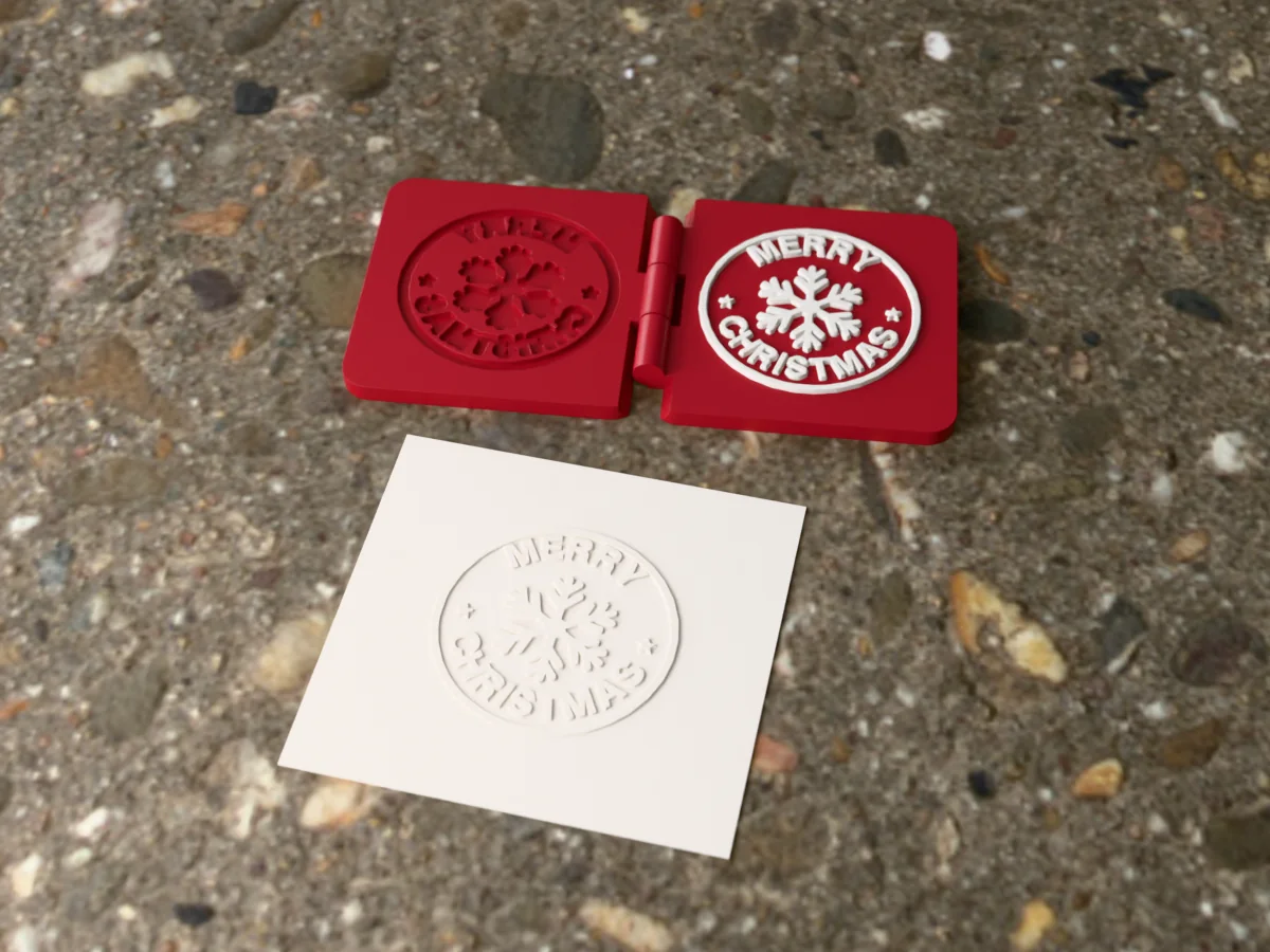 3D render of the printed Merry Christmas embosser, open flat on its hinge, with the raised die and the matching cavity, next to a card embossed with its mark