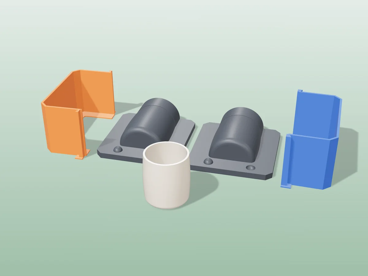 3D render of two printed plaster-mold housings for a mug body, orange and blue shells beside charcoal bases, with a cream fired mug body in front