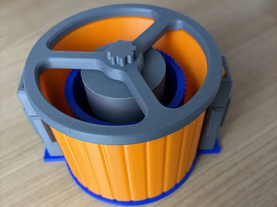 Assembled 3D printed vase mold on a wooden desk: orange ribbed outer shell on a blue base plate, with a grey inner core held centred by a grey spoked top ring and clamps on the seam