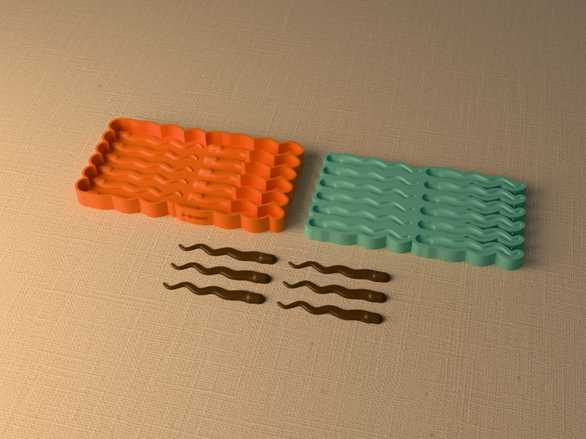 3D render of the printed caster for a twelve-cavity silicone ribbon leech lure mold beside the silicone mold it pours, with dark brown soft plastic leeches in front