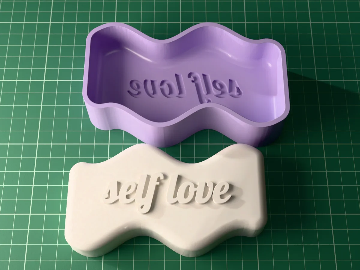3D render from above of a white wavy slab candle lying face up with "self love" in raised script, the silicone mold it is cast in behind it