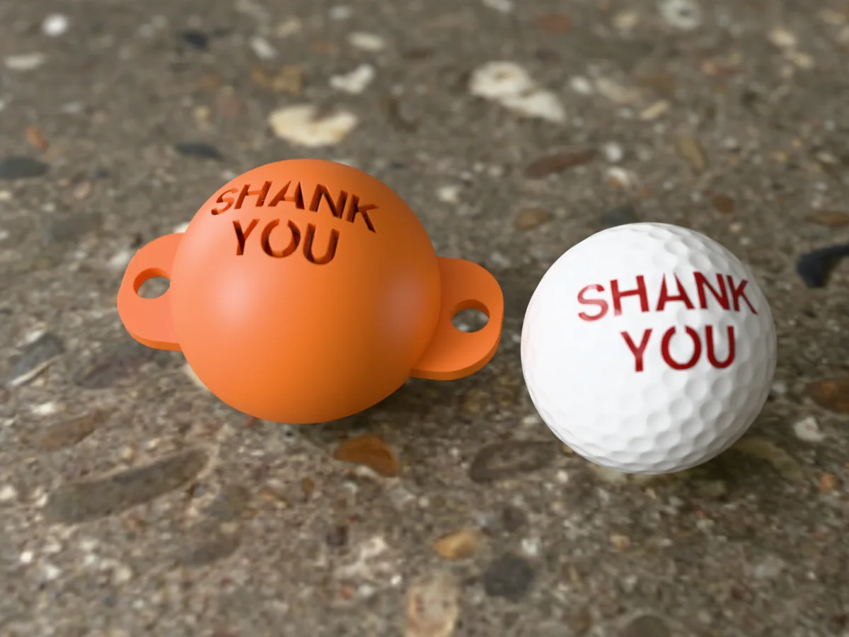 3D render of an orange 3D-printed golf ball stencil with SHANK YOU cut through it, sitting on a golf ball, next to a ball marked with SHANK YOU in red