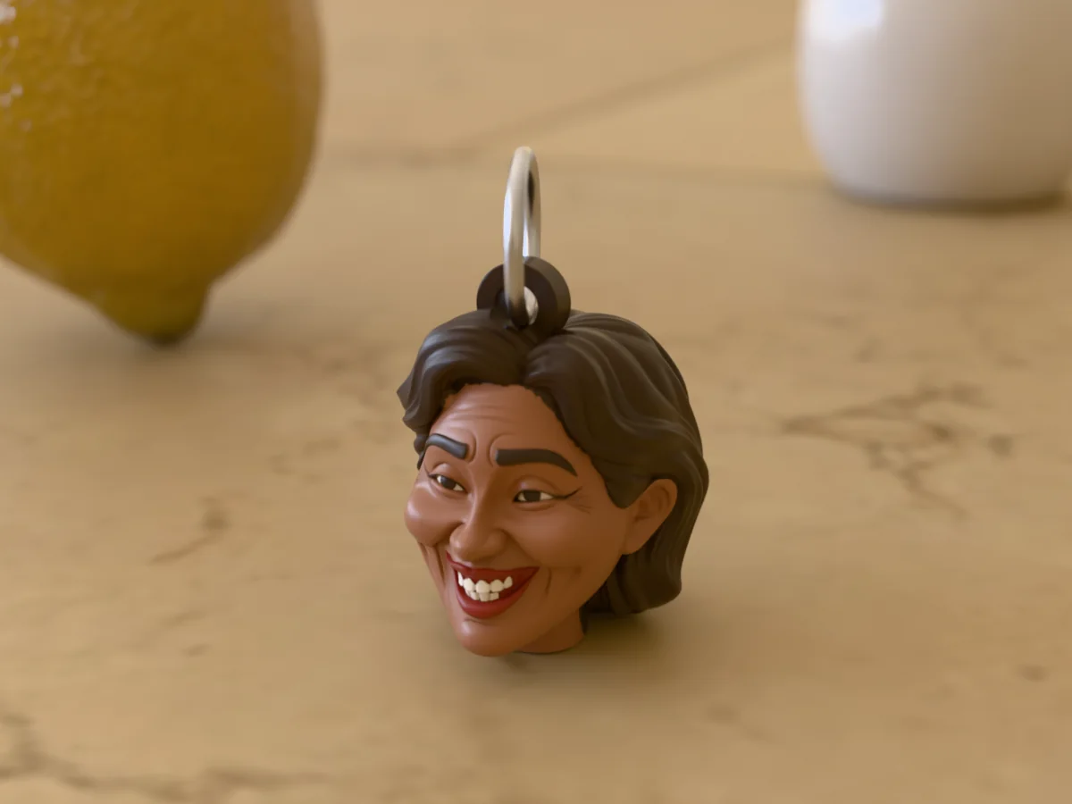 3D render of a 3D-printed head keychain of a smiling woman with long dark hair, painted in 5 colours, on a table
